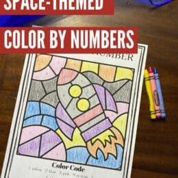 sample page colored in of space themed color-by-number sitting on a table with 3 primary crayons